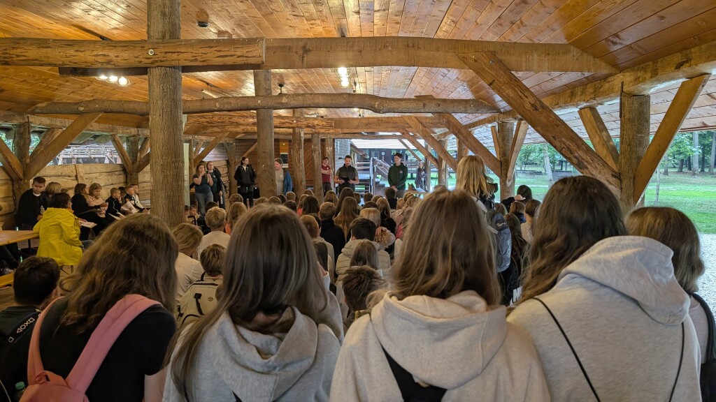 A large group of schoolchildren attends an educational gathering in a wooden pavilion.