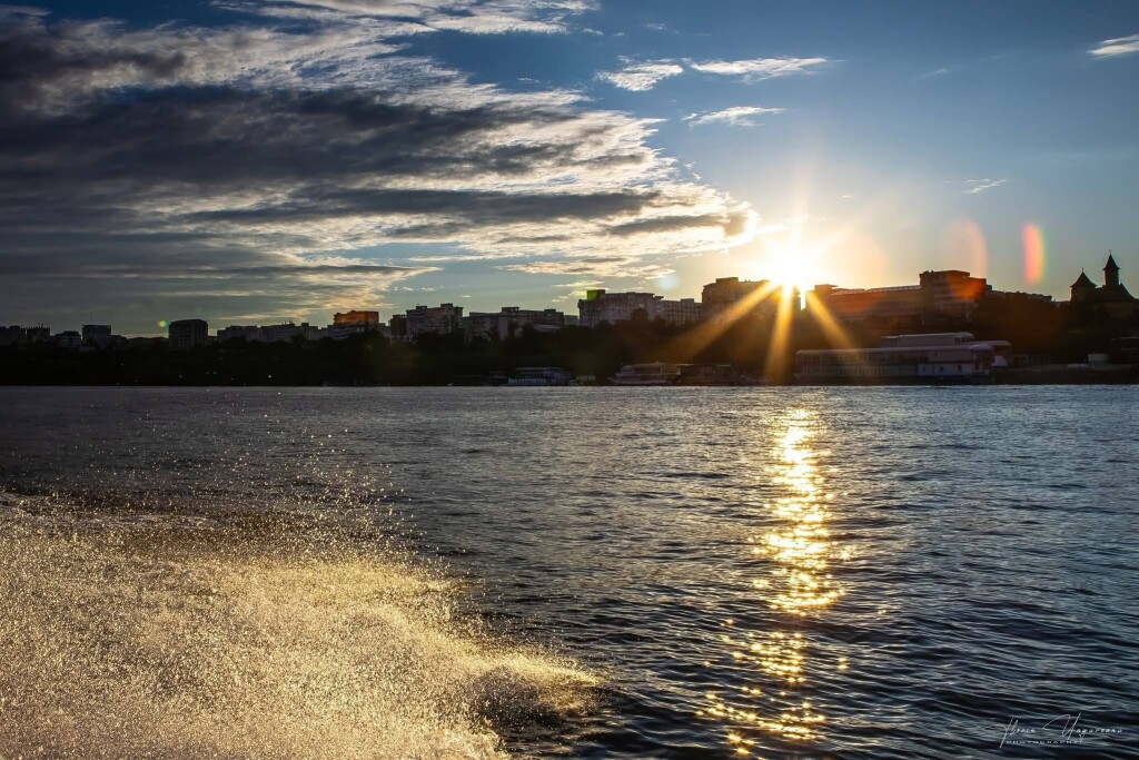 View across the Danube towards a city skyline at sunset, with sunlight reflecting on the river.