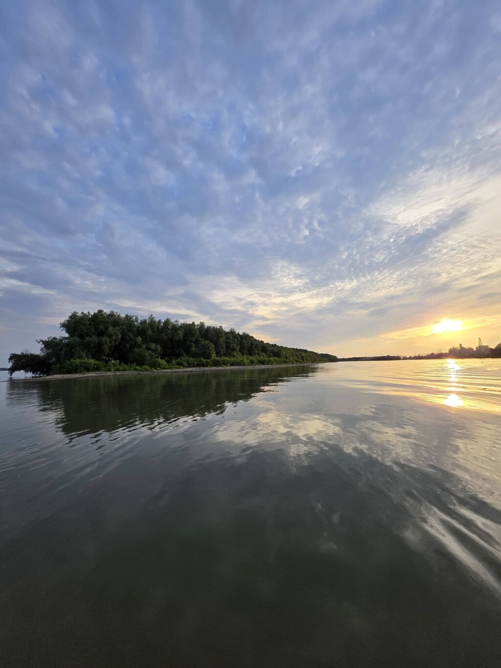 Danube river island with dense riparian vegetation at sunset, reflected in the calm water.